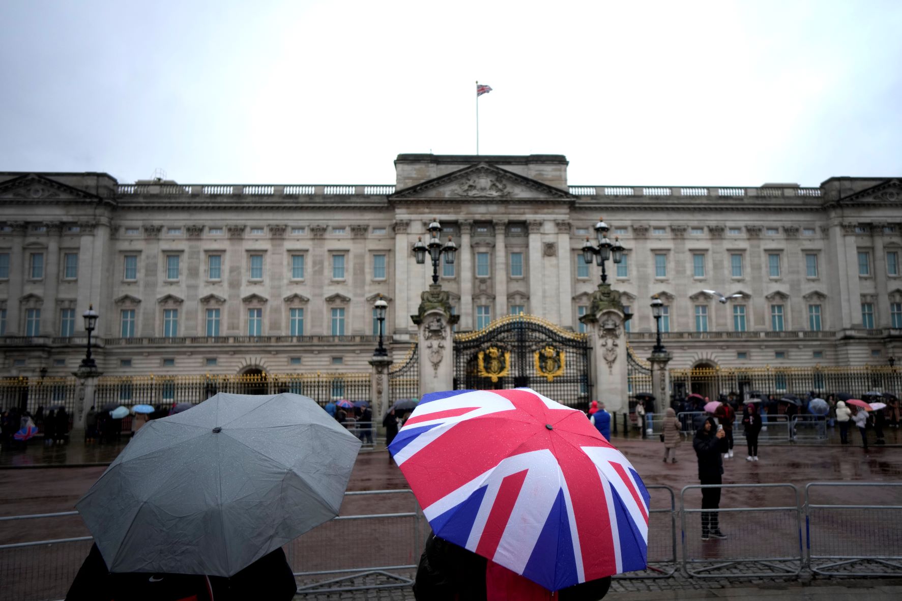سواح يحتمون من المطر بمظلة أثناء زيارتهم قصر باكنغهام في لندن بتاريخ 10 يناير 2023