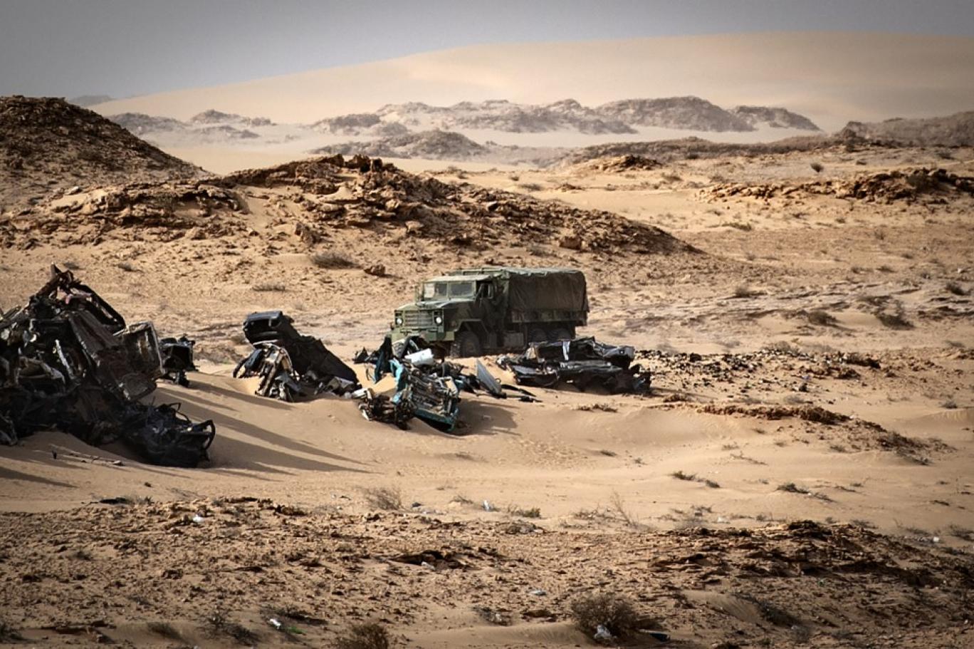 مركبة تابعة للجيش المغربي تمر أمام حطام سيارات في كركرات بالصحراء الغربية (أ ف ب)